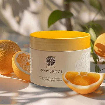 Assemble K - Play .Try .Glow Tiela Perfume Therapy Body Cream Shine 200g in a beige tub with a gold lid, featuring a citrus-floral-cedarwood scent.