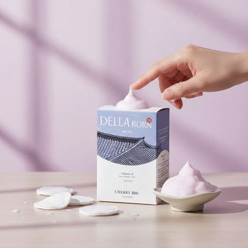 Assemble K - Play .Try .Glow Della Born Bubble Cleansing Pad box with pink foam and cotton pads on a wooden surface.