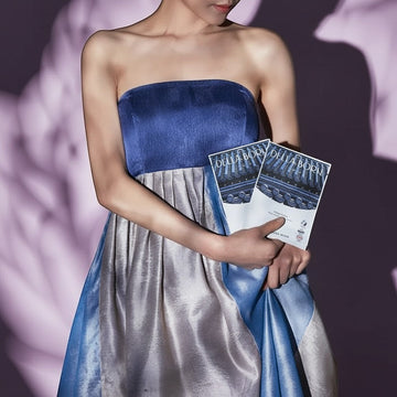 Assemble K Della Born Lotus Peel Mask, a hydrating facial treatment with lotus extract, presented by a model in a blue and silver strapless gown.