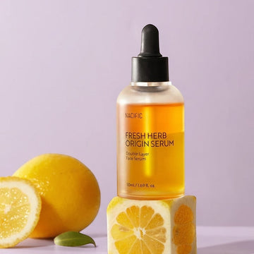 Assemble K - Play .Try .Glow Nacific Fresh Herb Origin Serum, a double-layer face serum in a clear bottle with a black dropper, featuring a golden liquid and citrus accents.