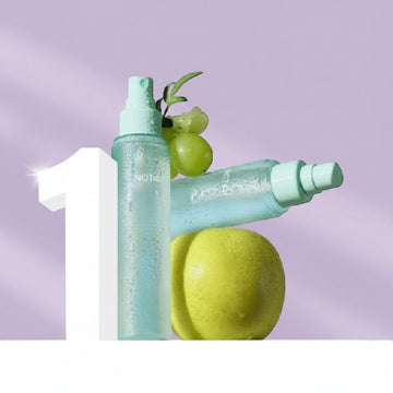 Assemble K - Play .Try .Glow NOT4U Soft Body Mist 115ml, a light blue spray bottle with water droplets, next to green grapes and a pear.