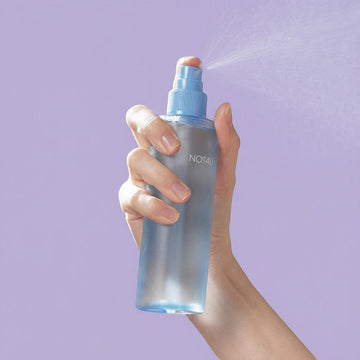 Assemble K - Play .Try .Glow NOT4U Clear Body Mist 200ml, a frosted blue bottle with a light blue spray nozzle, misting into the air against a bright blue background.