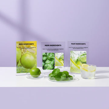 Assemble K - Play .Try .Glow product display featuring fresh limes, Centella leaves, and lemon water on a purple background