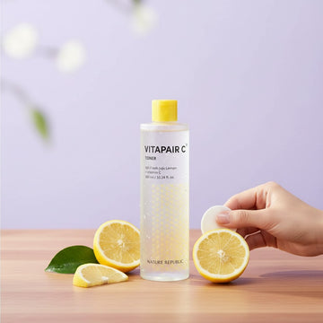 Assemble K - Play .Try .Glow NATURE REPUBLIC Vitapair C toner bottle with fresh lemon slices and a cotton pad on a table