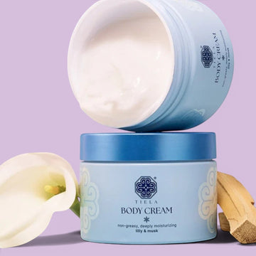 Assemble K - Play .Try .Glow Tiela Body Cream in a light purple jar with a blue lid, featuring a floral design and text indicating a coconut floral woody scent.