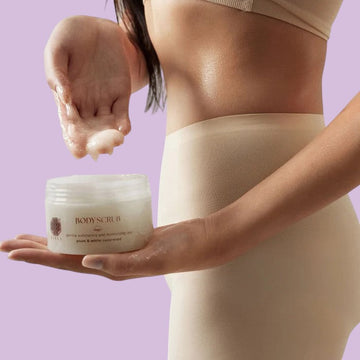 Assemble K - Play .Try .Glow Tiela Perfume Therapy Body Scrub Sunset 250g, a gentle exfoliating sugar scrub with a fruity-floral-woody scent, in a cream-colored jar with a burgundy lid, adorned with red flowers.