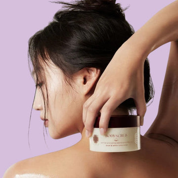 Assemble K - Play .Try .Glow Tiela Perfume Therapy Body Scrub Sunset 250g, a gentle exfoliating sugar scrub with a fruity-floral-woody scent, in a cream-colored jar with a burgundy lid, adorned with red flowers.