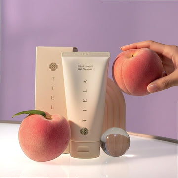 Assemble K - Play .Try .Glow Tiela Ritual Low pH Gel Cleanser in a white tube with a peach and decorative items.