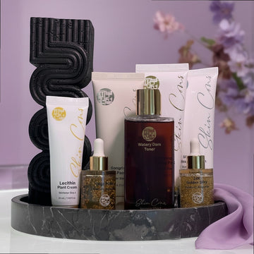 Assemble K - Play .Try .Glow Skinterior Step 2 Watery Dam Toner, a dark amber liquid in a glass bottle with a gold cap, part of a skincare set.